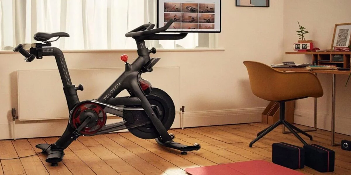A Peloton Bike+ set up in a home office, featuring its 24-inch rotating HD touchscreen turned towards a yoga mat for a seamless floor workout.